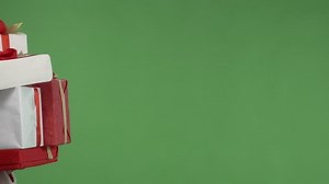 Female Santa helper carrying many red white gift boxes against green screen