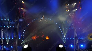 A circus show with tightrope walkers under the dome of the circus under the light of colorful spotlights. An acrobat girl sits on a rope splits under the dome of the circus.