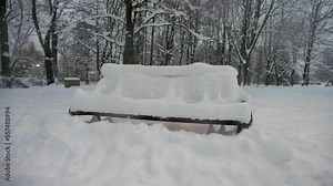 Snow-covered bench in the winter public park at twilight.