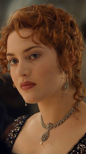 C A M A A L O T on Instagram: "“It’s not about the first look — it’s about that look. When your eyes find the one they already know.” Rose walks down the grand staircase in her elegant red gown, her white satin gloves catching the soft light. Jack waits below, his hand extended, ready to gently kiss hers. A simple, timeless moment of quiet elegance. The gown, designed by Deborah L. Scott, blends 1912 Edwardian sophistication with cinematic romance — delicate beadwork, sheer black lace details, a