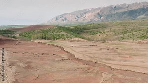 Aerial drone footage of beautiful vast sandy valley and green foothills of mountains. Wild nature for background design. Red soil and vegetation in highlands overviewing misty mountain.