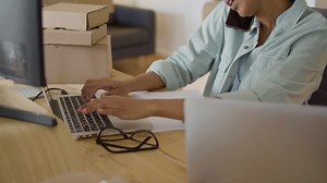 Young Black woman sitting at desk, working on computer and checking order via phone | Free Stock Video Footage