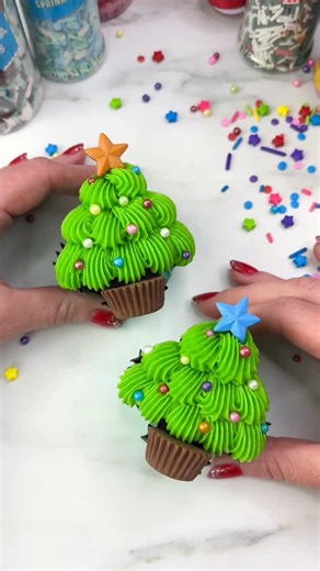 Wilton Cake Decorating on Instagram: "🎶Oh Christmas Tree🎶 You are so easy to decorate🎄Here’s how to decorate a cupcake to look like a cute Christmas Tree: 🎄Fill your liners half full and shape by adding two rolled up foil balls to the bottom to make the trunk, then add two folded pieces of foil to the sides to form a point 🎄Bake and cool then tint buttercream with green gel and use tip 32 to pipe the tree, finishing in a point at the top 🎄Decorate your cupcake with rainbow sprinkles, top w