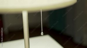 Woman Turns On Light. Closeup of Female Fingers Hand Pulling Cord from Table Lamp. Turning on Table Lamp. Light Turns On in Room, Close up.