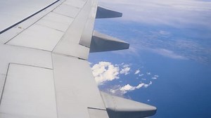 View From Airplane Window While Flying Over Ocean and Distant Land During Sunny Day. Looking out plane window, breathtaking view unfolds with vast blue ocean and fluffy white clouds