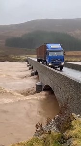 Narrow Escape as Bridge Collapses in Flood Isle of Skye, Scotland — October 14, 2025 A heavy-duty truck narrowly avoided disaster on Monday as it crossed a historic stone arch bridge in the Scottish Highlands during a period of intense flash flooding. The river below, swollen with sediment and debris, put immense pressure on the centuries-old structure as the water level reached the top of the arches. The dramatic footage shows the blue Volvo truck cautiously making its way across the span while