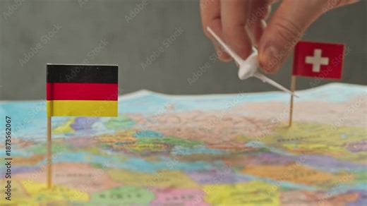 Toy airplane flying from Germany to Switzerland above colorful world map, symbol ski holidays, business trips, scenic flights and frequent regional air travel.