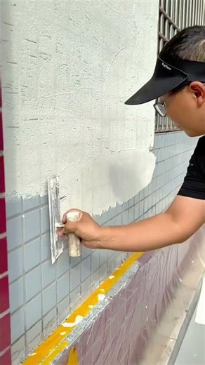 Applying white plaster coating over tiled exterior wall surface