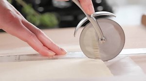 Macro. Chef cutting dough into strips with a pizza cutter, camera moves with the cutter, working in the kitchen. Making dough, cheese sticks from dough, puff pastry snacks. Close-up, side view