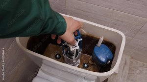 The repairman installs cistern fittings in the toilet tank, closes the lid and turns the button. and presses it, checking the working condition. Home plumbing repair