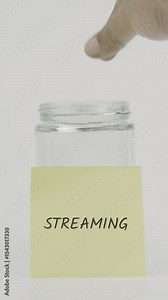 Streaming text or word on a yellow sticky note attached to a glass jar. A hand inserts a coin, symbolizing hidden goals or confidential savings. White background, vertical screen