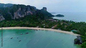 Flying away from rilays beach at krabi region in thailand. Beautiful colorful excotic paradise natur with palms and little taxi boats and people at the beach - cinematic aerial drone shot - outtro ad