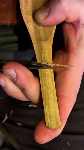 carefully carving of a wooden spoon using a sharp tool to create a smooth surface with very neatly