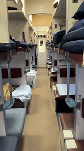 Sleeping berths in a second-class train carriage with neatly arranged bedding and dim ambient lighting.