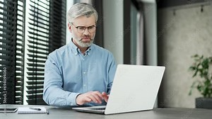 Frustrated mature gray haired bearded businessman having problems with software or service on laptop computer in business office. Worried disappointed man complains about a bad internet connection