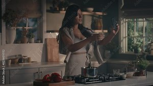 Pretty woman cooking soup on stove at kitchen. Close up of housewife preparing dinner at home. Young woman tasting soup on spoon at modern kitchen in slow motion, talking on phone, taking photos