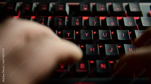 man's hands typing on a black illuminated computer keyboard. selective focus.