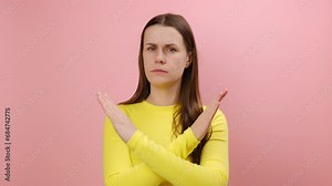 Serious young woman crossing hands, showing x sign, stop gesture, warning of end finish, forbidden way, wearing sweater, isolated on pink background wall in studio. Definitely no, prohibited access