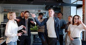 Mixed-races men and women celebrating end of working week in office. Multiethnic coworkers dancing and having fun ar workplace. Young team of company employees having party. Funny moves.