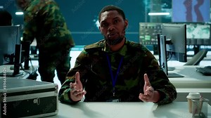 Military intelligence expert conducts a strategic teleconference connection in a modern command post, utilizing real time data on multiple screens for communication and decision making. Camera A.