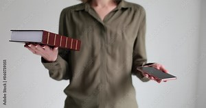 Woman intuitively measures weight of thick book and mobile phone in hands. Woman lifting objects compares traditional and modern technologies slow motion