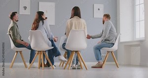 Team of people sitting in a circle, communicating during a meeting or psychology session with coach or trainer. Diverse group engaged in discussion, highlighting teamwork and collaboration.