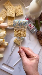 These Spring-inspired Rice Treat Pops are as easy as they are stunning! Perfect for a sunny day snack or as a sweet addition to your dessert table, they’re fun to make and delicious to eat. The Cake Mate Pearlescent Sugar Crystals add that magical sparkle for a truly festive touch! Ingredients: *6 pre-made rice cereal treats (store-bought or homemade) *1 cup vegan white chocolate chips (or regular, as preferred) *1 teaspoon coconut oil *Cake Mate Pearlescent Sugar Crystals *6 lollipop sticks Ins