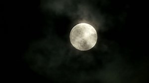 The Full Moon shines brightly in the cloudy night sky, creating a mystical backdrop