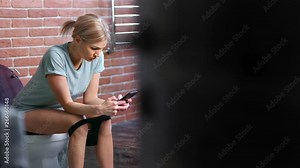 Beautiful confident young woman sitting on toilet chatting using smartphone medium long shot