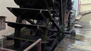 An old waterwheel or turbine drives an electric generator near a natural flowing water.