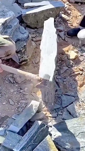 Worker splitting large stone manually using heavy hammer tool