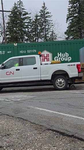 CN highway-railroad truck rolls West past a stopped container in well car train