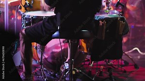 Close-up of drummer's feet pressing pedals of bass drum and hi-hat. Man playing drums fast at a concert. Rear view. Drummer on stage surrounded by lighting effects