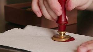 Premium stock video - Pressing a wax seal into hot wax on a piece of parchment, sealing the letter