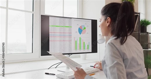 Analyst woman reviews data charts on computer monitor. She reviews an office dashboard and spreadsheet, interprets metrics, and prepares a report for planning. Clear data driven decision concept.