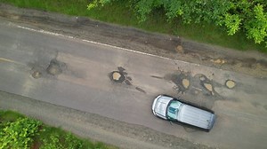 AERIAL TOP DOWN: Car driving over big road pits on countryside road in tropics. Careful drive while travelling along countryside road in tropical destination. Bad road maintenance in third world.