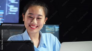 Close Up Of Asian Female Programmer Looking At Tablet And Writing Code By A Laptop Using Multiple Monitors Showing Database On Terminal Window Desktops In The Office Stock Video
