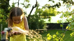 Happy kid girl playing by hand with garden sprinkler , summer outdoor water fun in the backyard at home, splash on sunny day.