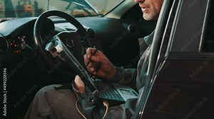 Service, repair, maintenance concept. Mechanic man sitting inside car with laptop making diagnostics at auto service. Interactive Diagnostics Software on an Advanced Computer. Troubleshooting engine.