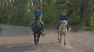 Man and woman riding horses together. Couple learning to ride horse. Male and female equestrians walking on horse racetrack. Steadicam shot.