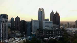 4K Ariel Drone Shot Passing Around Beautiful Skyline Buildings In Charlotte, North Carolina. USA. Golden Sun Shining Through Gaps Of Buildings. Area Covered With Trees. Golden Yellow Sky.