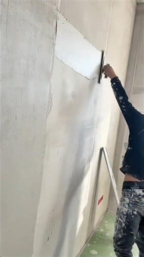A plasterer is using a float to apply a large, smooth coat of white leveling compound onto a light