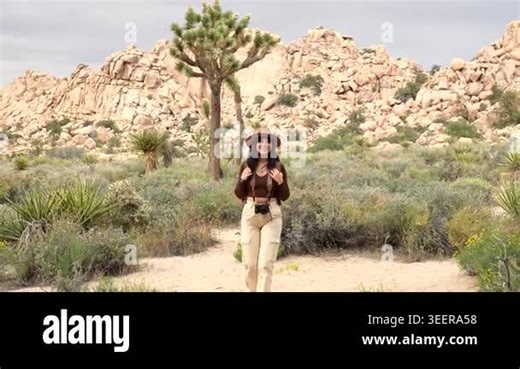 Young smiling woman with a hat, backpack, and camera enjoying a trekking adventure on a hiking trail through the beautiful desert landscape of joshua tree national park in california Stock Video Footage - Alamy