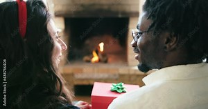 Closeup young couple sit and open gift box on sofa in front of fireplace