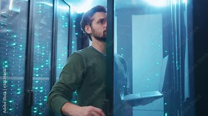 Young data center engineer opening rack server network checking hardware and system performance typing data on laptop keyboard coworking with colleague.