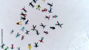 Aerial: a large group of snow angels. top view on skiers making angels in the snow and lazing in the shape of a random circle. young people in bright sports clothes represent snowangel