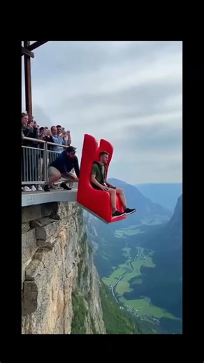 Red Dragon on Instagram: "This exhilarating video captures a high-altitude stunt involving a base jumper and a large inflatable cushion. Breakdown of the Stunt The Launch: A man is seated on a red chair-like device at the edge of a sheer cliff. The Drop: Another person pushes the chair off the edge, sending the jumper into a freefall over a lush valley. The Impact: The jumper falls onto a large, white inflatable bag positioned on a rocky ledge below. The Rebound: Upon hitting the bag, the jumper