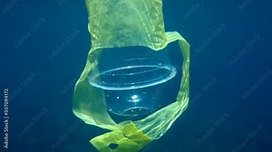 Underwater video of plastic cocktail cup with a plastic holder swimming in crystal blue water in sun rays. Environmental plastic pollution problems concept. World ocean day. Trash and waste in the sea
