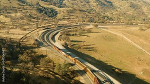 The aerial camera shoots a train going in to the south entrance of the rail loop from 150 feet above the tracks. The aerial camera follows the trail rolling towards the crisscross section of the loop.