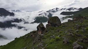 A drone overflying next to a cliff overlooking a mountainous landscape